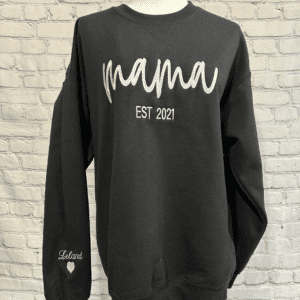 Close-up of a cozy gray sweatshirt with delicate embroidery that reads 'Mama' accompanied by the established year, celebrating motherhood in a personalized and heartfelt way.